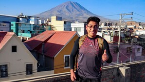 Una persona de pie en la azotea con una mochila, contemplando un paisaje urbano con edificios de colores y una montaña al fondo.