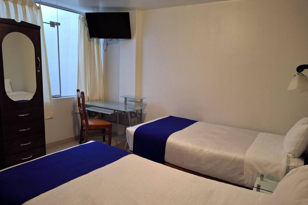Une chambre d’hôtel avec deux lits, un bureau, une chaise, une télévision et une armoire.