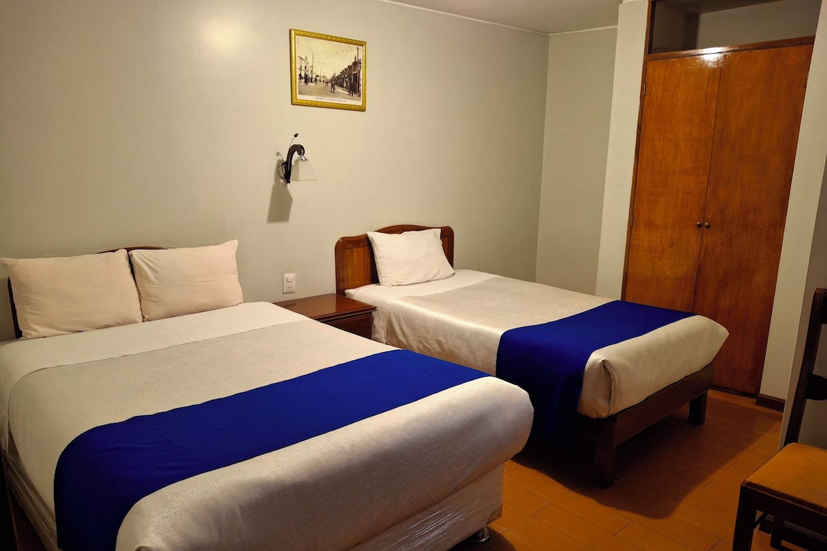Une chambre d’hôtel avec deux lits, une armoire en bois, une petite table et un tableau accroché au mur.