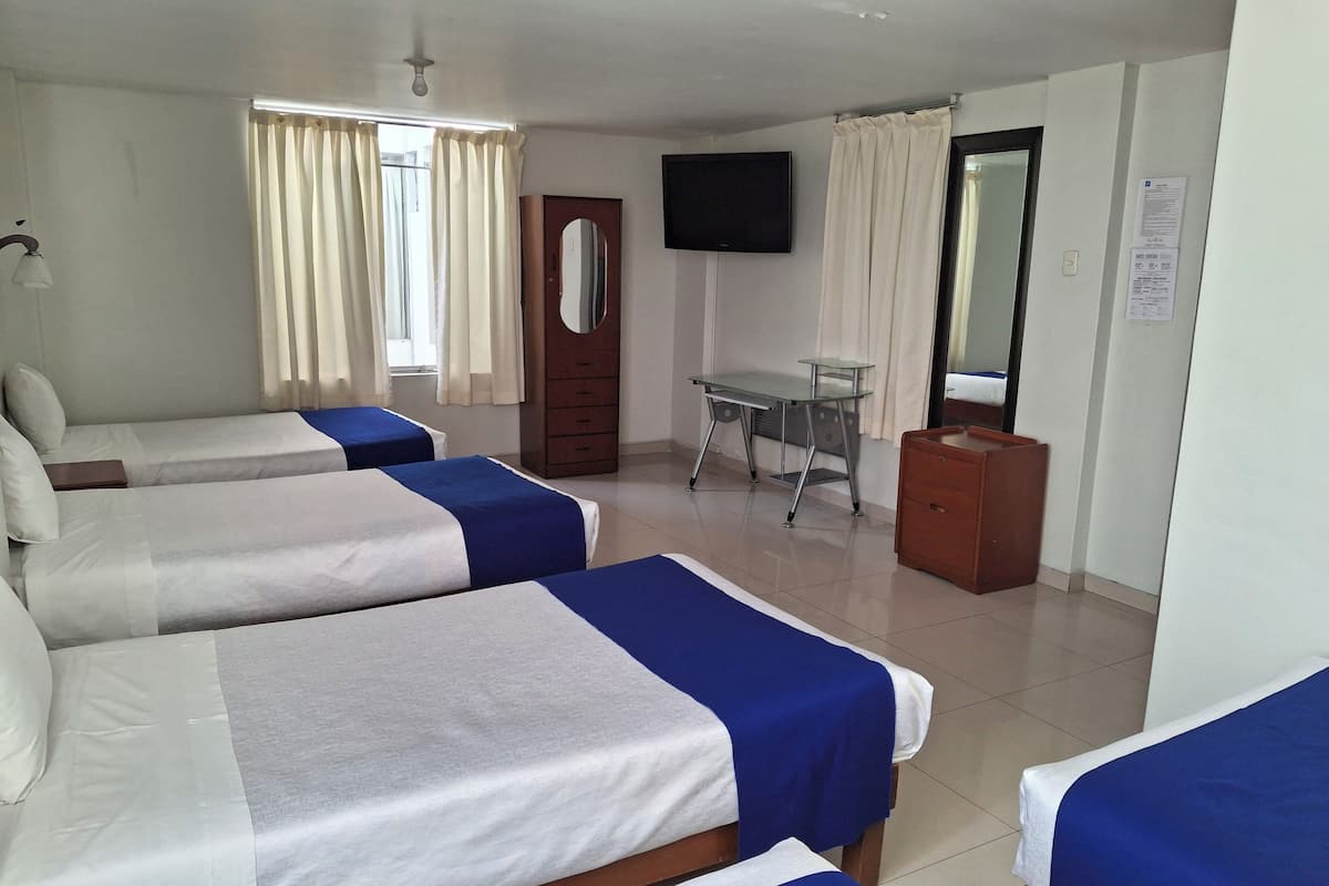 Une chambre d’hôtel avec trois lits simples, un bureau, une chaise, une télévision et un miroir.