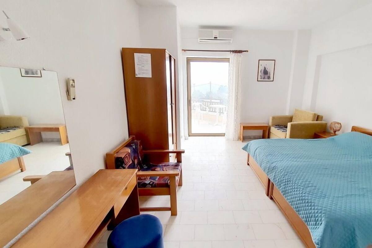 A hotel room with a bed, a desk, a chair, a wardrobe, and a view of the outside.