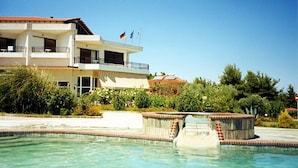 A two-story hotel with a swimming pool, surrounded by greenery and flags. - Hotel Pashos (Kriopigi)