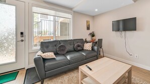 A modern living room with a black leather sofa, a wooden coffee table, and a flat-screen TV mounted on the wall.