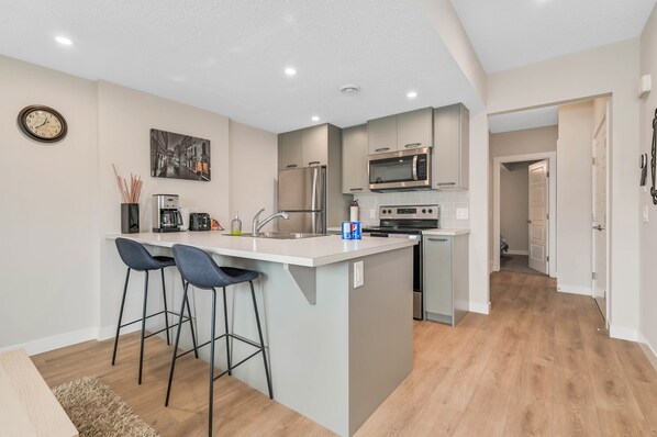 A modern kitchen with a central island, bar stools, stainless steel appliances, and a clock on the wall.