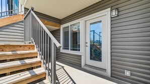A wooden deck with a metal railing, a door with a glass panel, and a window with a view of a bridge.