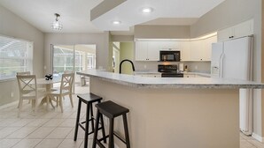 Une cuisine moderne avec des meubles blancs, un îlot central doté de tabourets, et un coin repas avec une table et des chaises.
