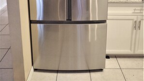 A stainless steel refrigerator in a kitchen with white cabinets and a tiled floor.