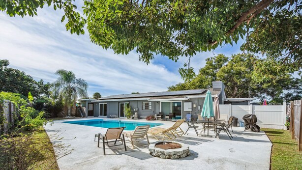 A backyard with a swimming pool, lounge chairs, a fire pit, and a covered patio area.