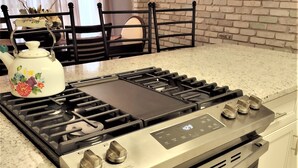 A kitchen with a stainless steel stove, a kettle, and a brick wall.
