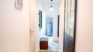 A narrow hallway with a bench, a refrigerator, and a hanging light fixture.