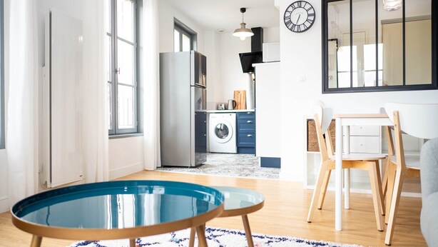 A modern kitchen with a washing machine, a dining area with a table and chairs, and a large window providing natural light.
