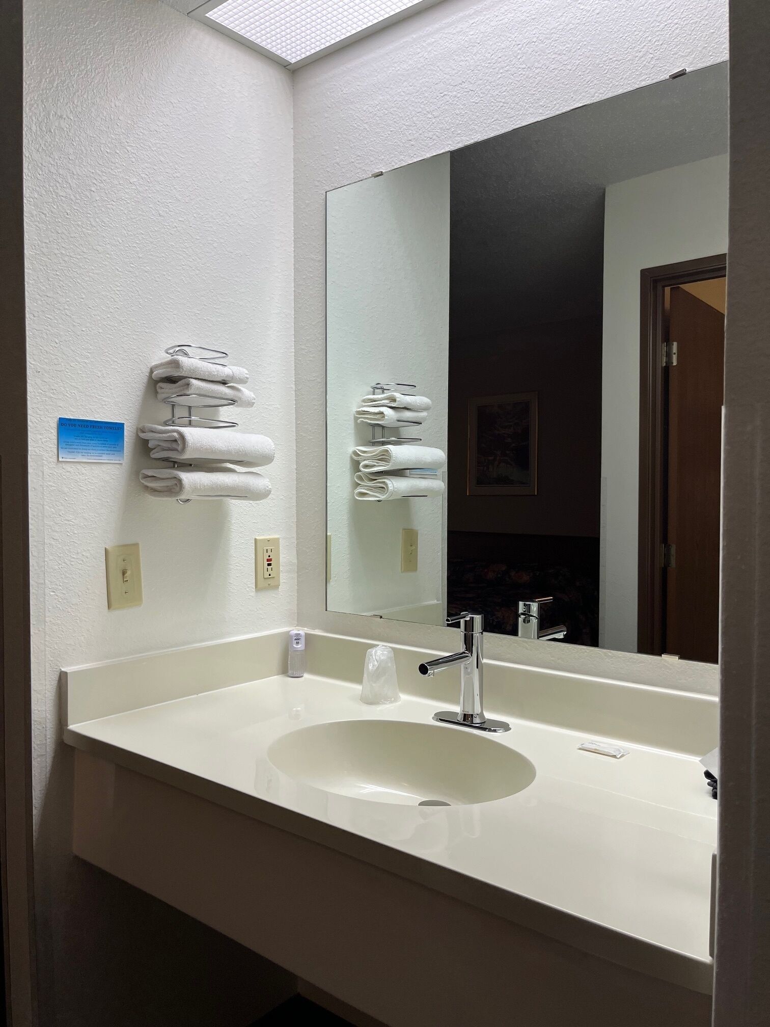 Un baño de hotel con un lavamanos blanco, un espejo grande y toallas dobladas en un perchero.