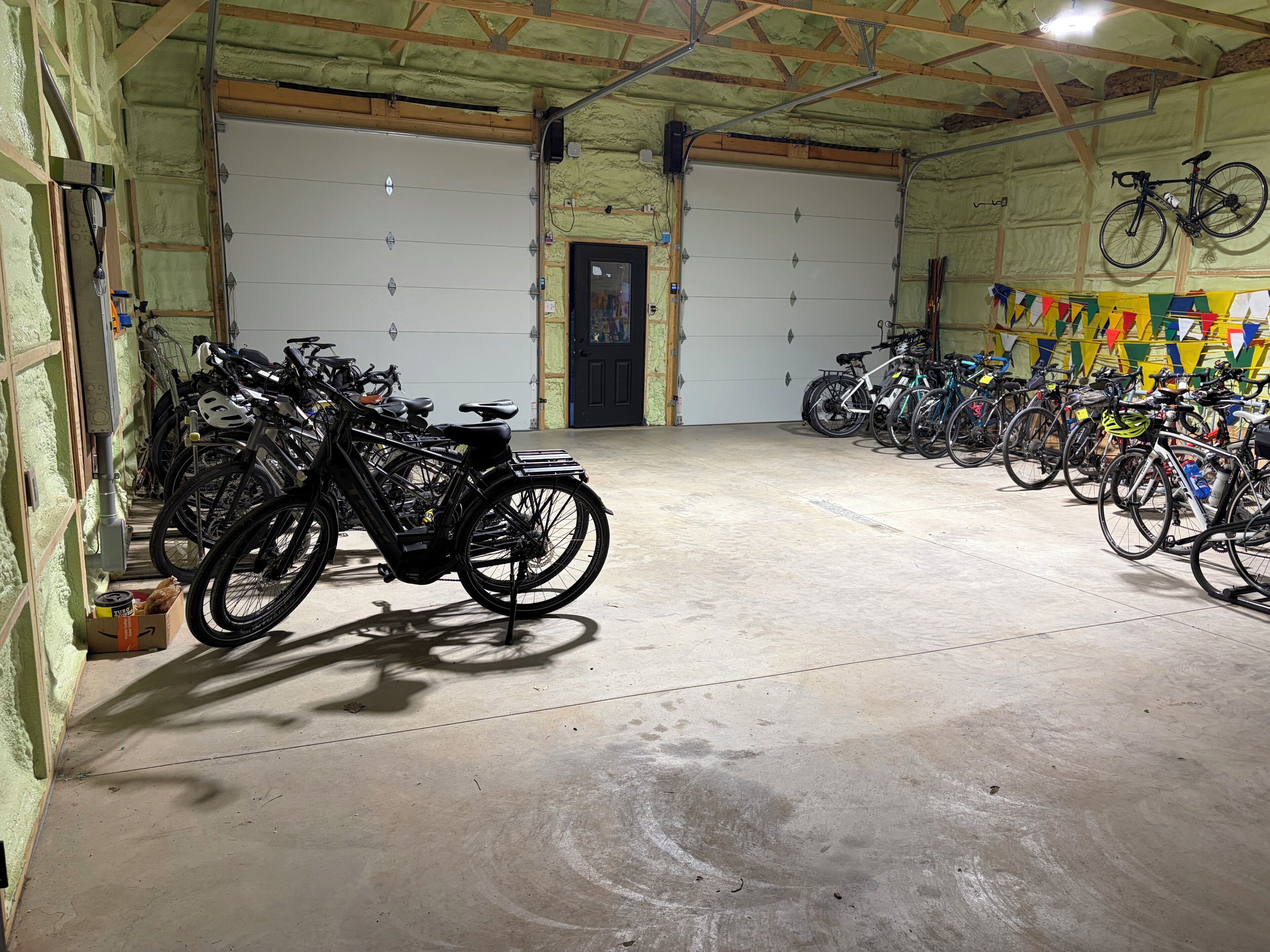 Amplio espacio interior con varias bicicletas estacionadas contra las paredes, piso de concreto y dos grandes puertas de garaje.