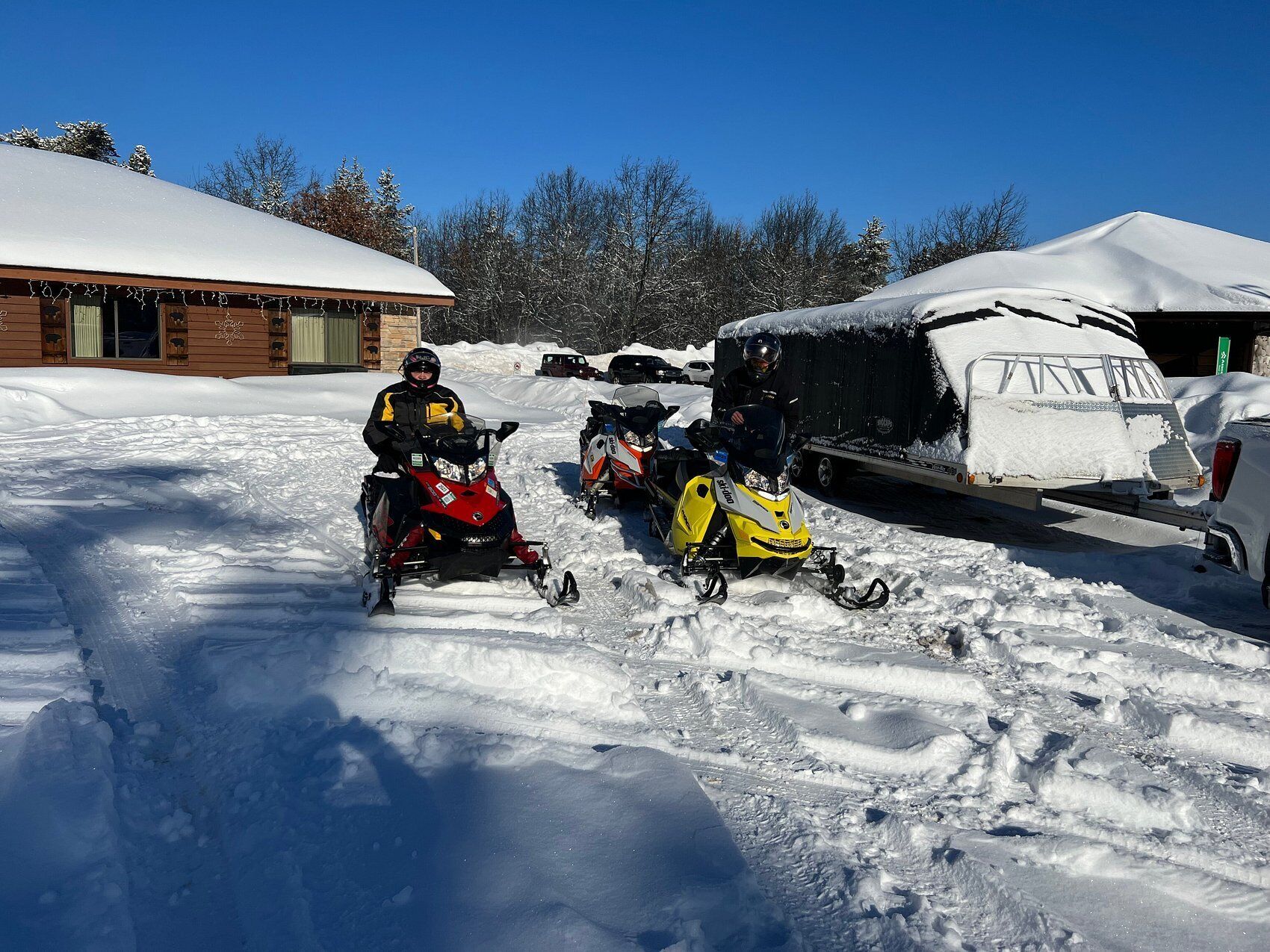 A snow-covered landscape with two snowmobiles parked in front of a building.