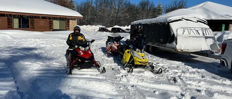 A snow-covered landscape with two snowmobiles parked in front of a building.