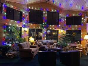 Interior acolhedor de cabana com paredes de madeira, lareira e decorações natalinas festivas.