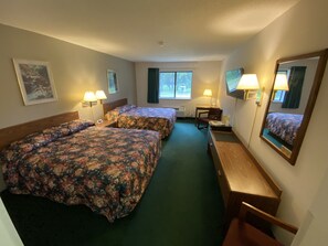 Quarto de hotel com duas camas, uma escrivaninha, uma cadeira, um espelho e uma janela com cortinas.