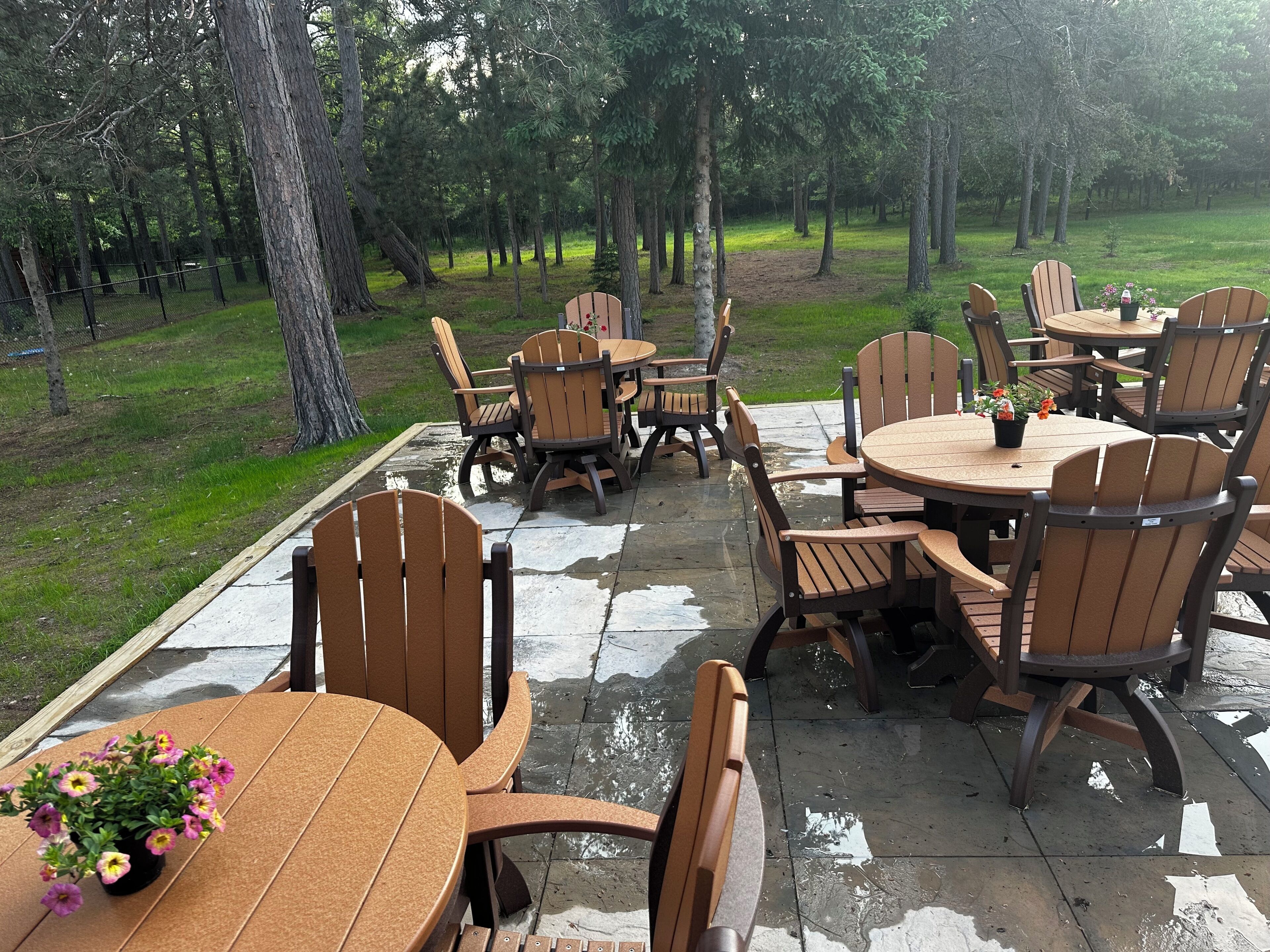 Eine Terrassengaststätte mit Holztischen und -stühlen, umgeben von einer Rasenfläche und Bäumen.