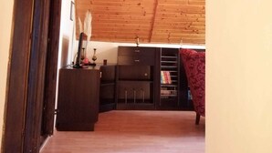 A wooden ceiling, a dark wooden cabinet, and a red patterned chair in a room with a wooden floor.
