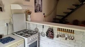 A compact kitchen with a gas stove, oven, and a white refrigerator. There is a white brick backsplash, a clock, and a vintage-style wall hanging.