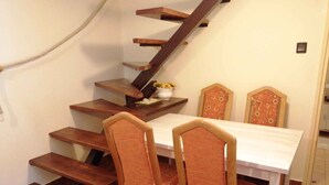 A dining area with a wooden staircase leading to an upper level, a white table, and two chairs with patterned backs.