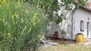 A white building with a sloped roof, a wooden chair, and a yellow planter.