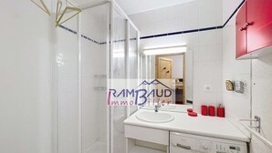 Een moderne badkamer met een glazen douchecabine, een witte wastafel, een wasmachine en een rode kast.