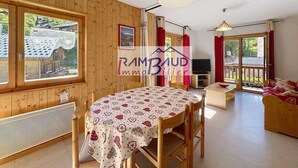 Een houten chalet met een eethoek, een televisie en een balkon met rode gordijnen.