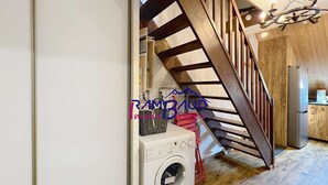 A laundry area with a washing machine, a drying rack, and a wooden staircase leading to a kitchen area.