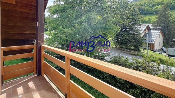 A balcony with a wooden railing overlooking a lush green landscape and a small house in the background.