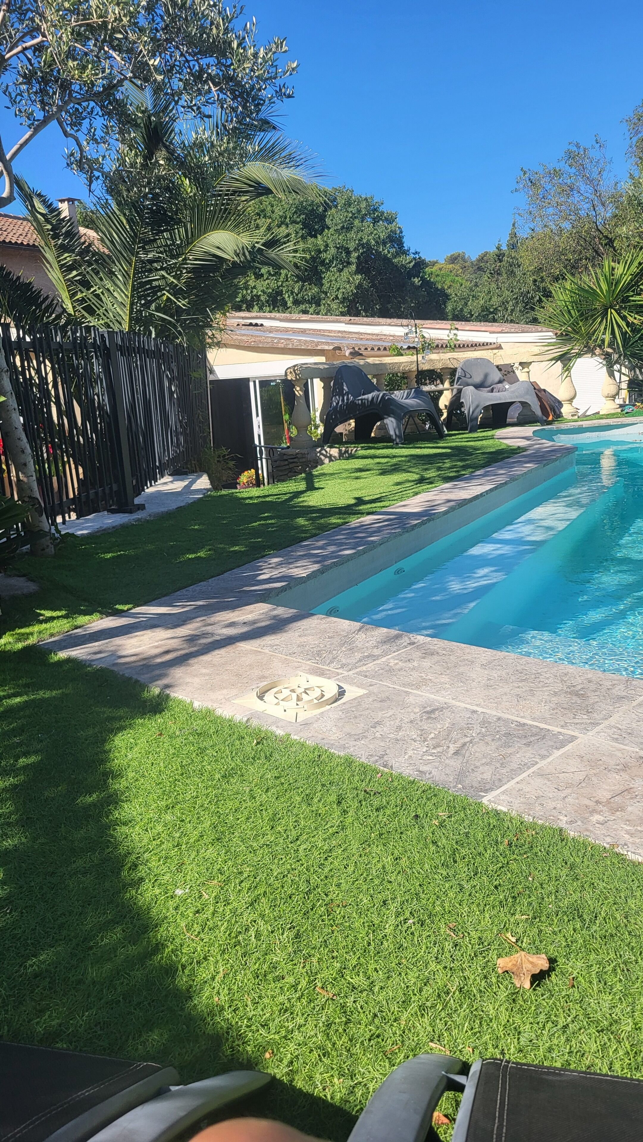 A backyard with a swimming pool, a stone pathway, and a fenced area with outdoor furniture.