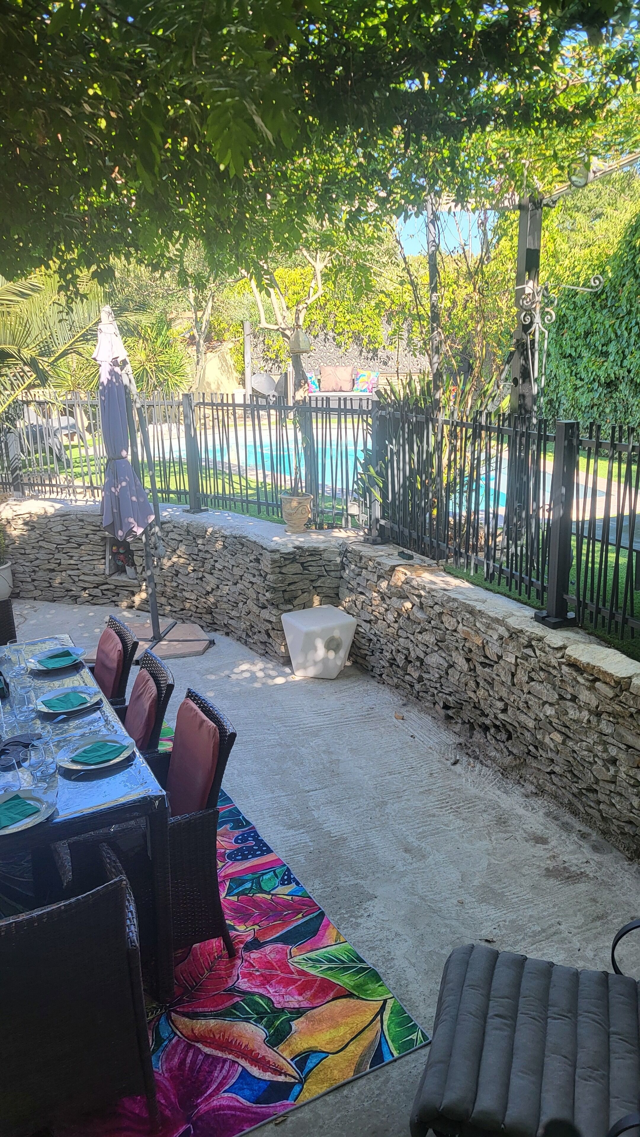 Een terras buiten met een stenen muur, een zwembad en een eethoek met vier stoelen en een tafel.
