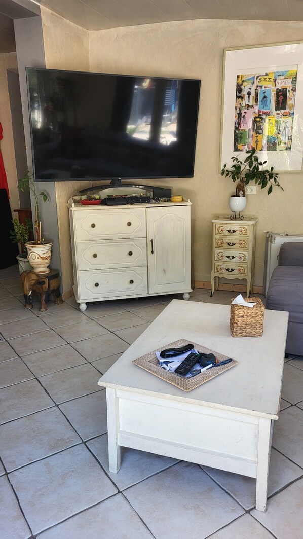 A living room with a white coffee table, a flat-screen TV, a cabinet, a small side table, and a framed picture on the wall.