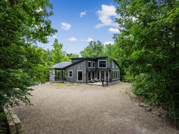 A modern house with a gravel driveway, surrounded by lush greenery.