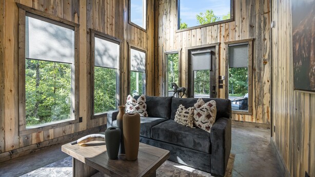 A wooden interior with large windows, a sofa, and a table with vases. - Romantic Cabin, Hot Tub, Fire Pit, Pets, Blackwater (Broken Bow)