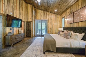 A wooden-paneled bedroom with a large bed, a television, and a brick-patterned console table.