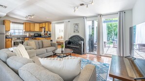 Ein modernes Wohnzimmer mit Sofa, Couchtisch und Kamin. Eine Küche mit Holzausstattung und ein Essbereich mit Tisch und Stühlen sind ebenfalls zu sehen.