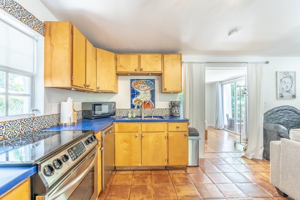 Compact kitchen with microwave, stove, and sink, featuring a tiled backsplash and window.