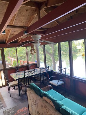 A dining area with a table and chairs, a ceiling fan, and large windows with a view of trees and a body of water.