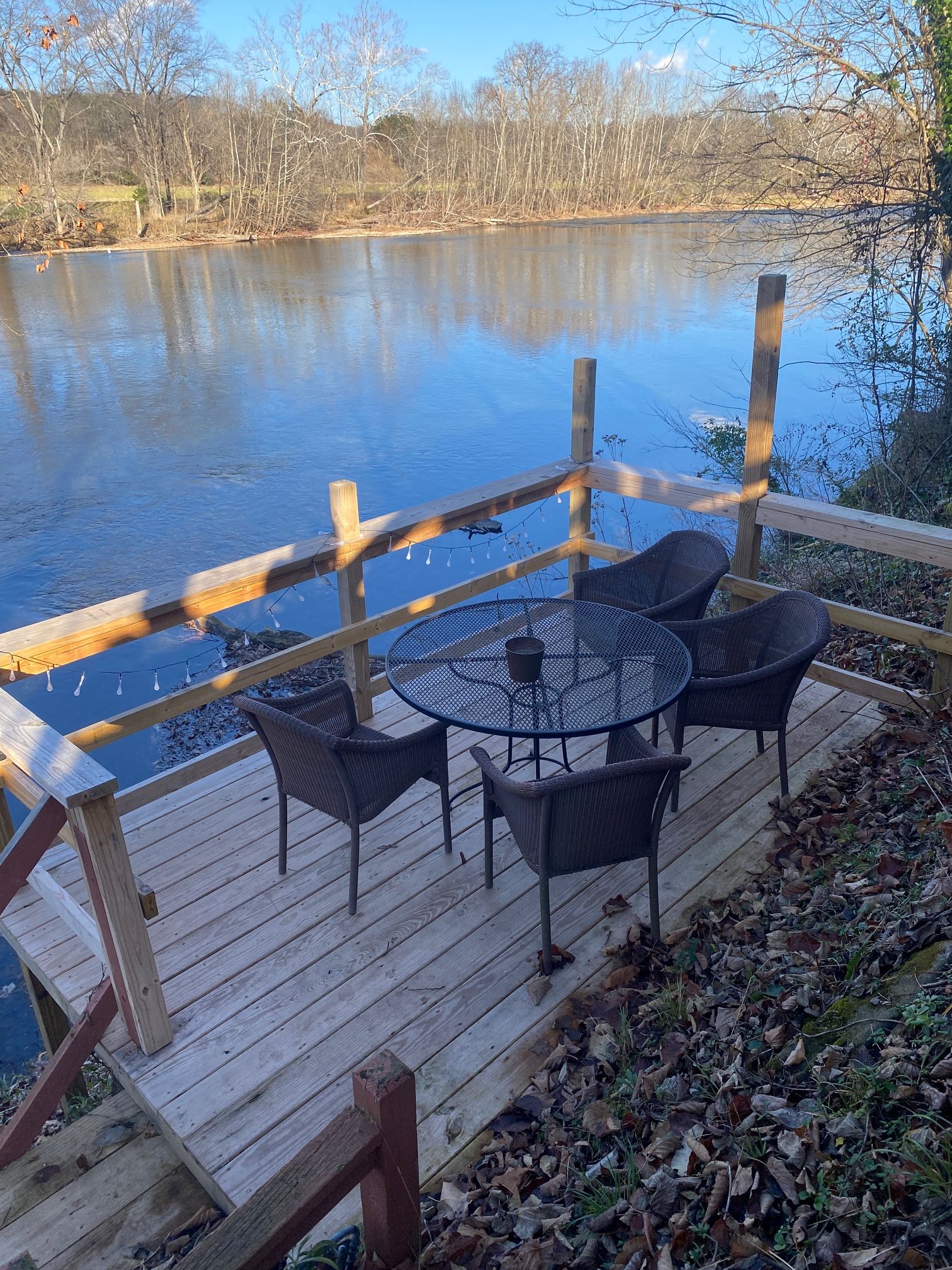 Terraza de madera con mesa y sillas con vista a un cuerpo de agua.