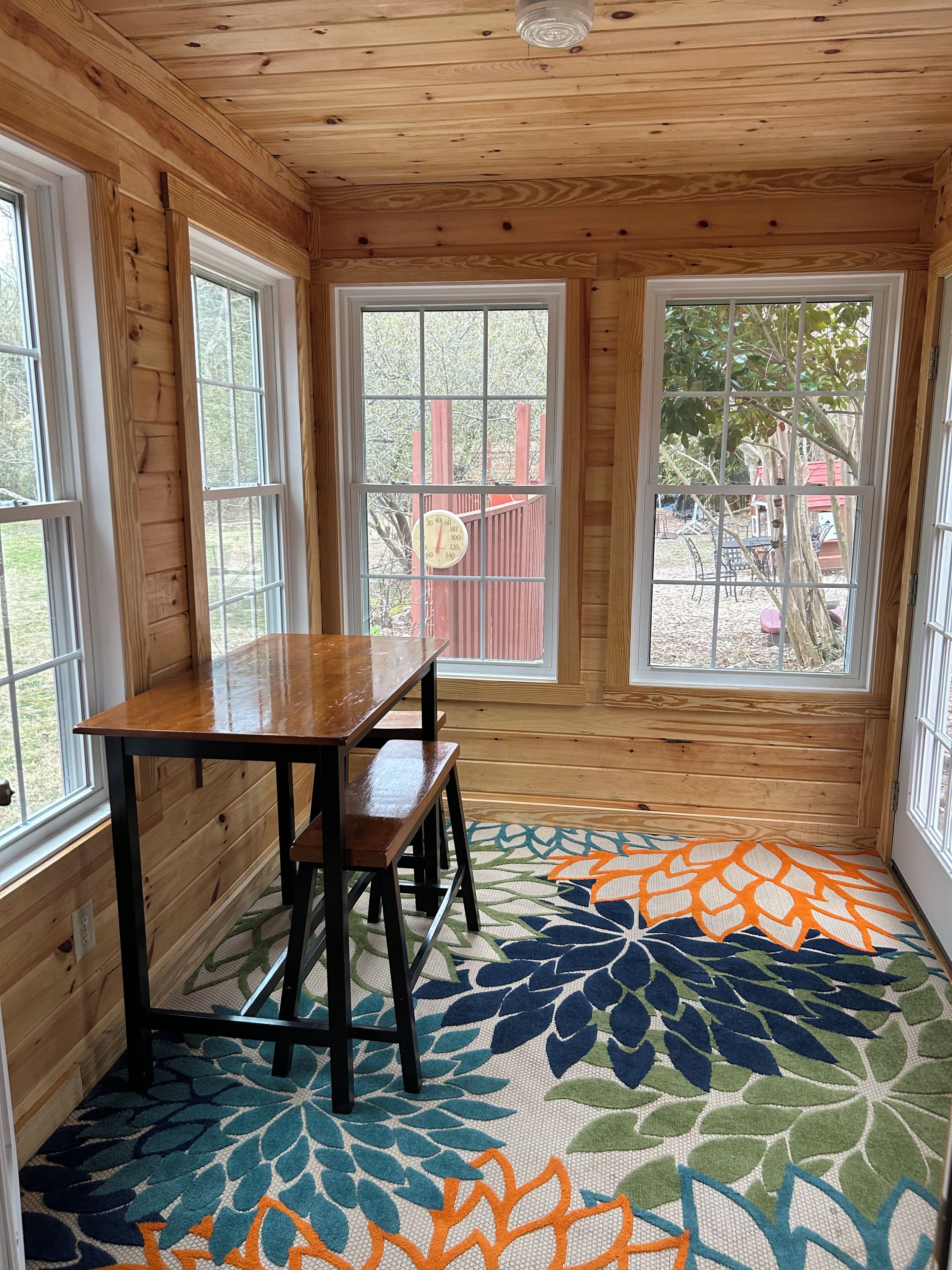 A room with a wooden interior, a table with chairs, and large windows with a view of a playground.