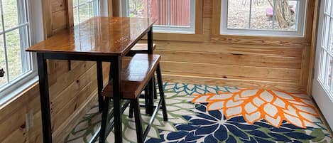 Een kamer met houten details, een tafel met stoelen en grote ramen met uitzicht op een speeltuin.