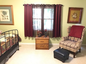 A bedroom with a bed, a dresser, a chair, and a window with curtains.