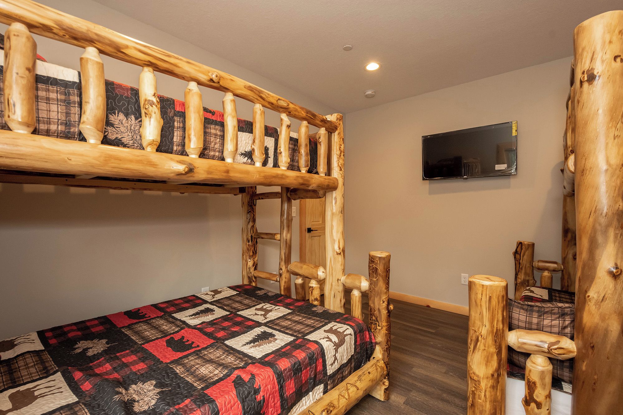 Een stapelbed met een gewatteerde spreidek, een houten hoofdbord en een televisie aan de muur.