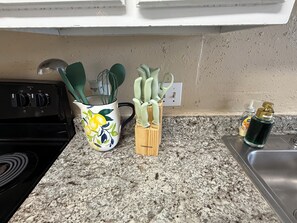 A kitchen with a granite countertop, a stove, a colorful pitcher, a wooden utensil holder, and a soap dispenser.
