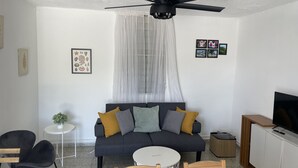 Ett modernt vardagsrum med en mörkgrå soffa, en takfläkt, ett litet runt bord och en tv som står på ett skåp.