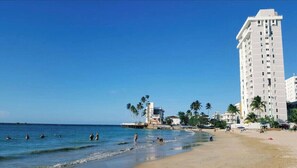 A beach with a tall white building, palm trees, and people swimming.