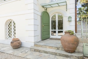 A building with a white facade, a green door, and a large terracotta pot on the steps.