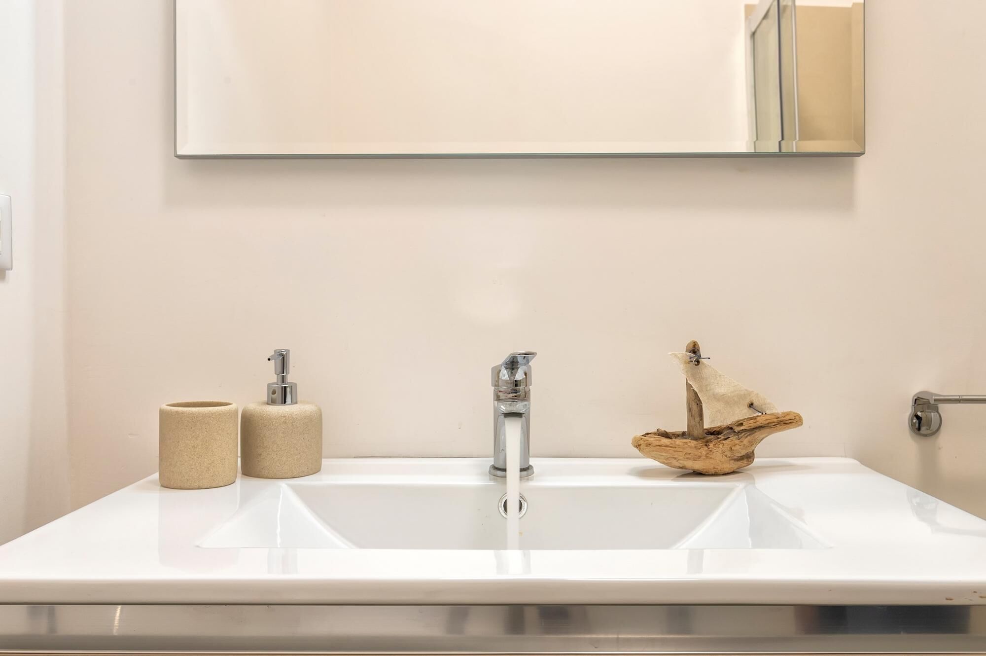 A bathroom with a white sink, a mirror above it, and two rolls of toilet paper on the counter.