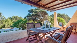 Un patio al aire libre con mobiliario de madera y una mesa, rodeado de árboles y un cielo despejado.